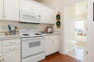 Kitchen with white appliances, white cabinets, light countertops, and dark wood-style flooring