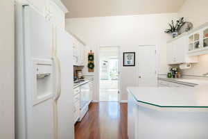 Kitchen with light countertops, white appliances, white cabinetry, dark wood-type flooring, and a peninsula