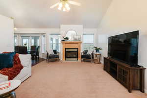 Living room with a fireplace with flush hearth, carpet, a ceiling fan, and high vaulted ceiling