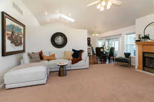 Carpeted living room with lofted ceiling, a fireplace with flush hearth, a chandelier, a skylight, and ceiling fan