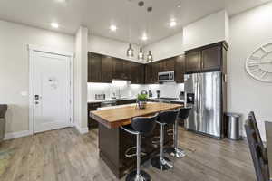 Kitchen featuring dark brown cabinets, wood counters, stainless steel appliances, pendant lighting, and tasteful backsplash