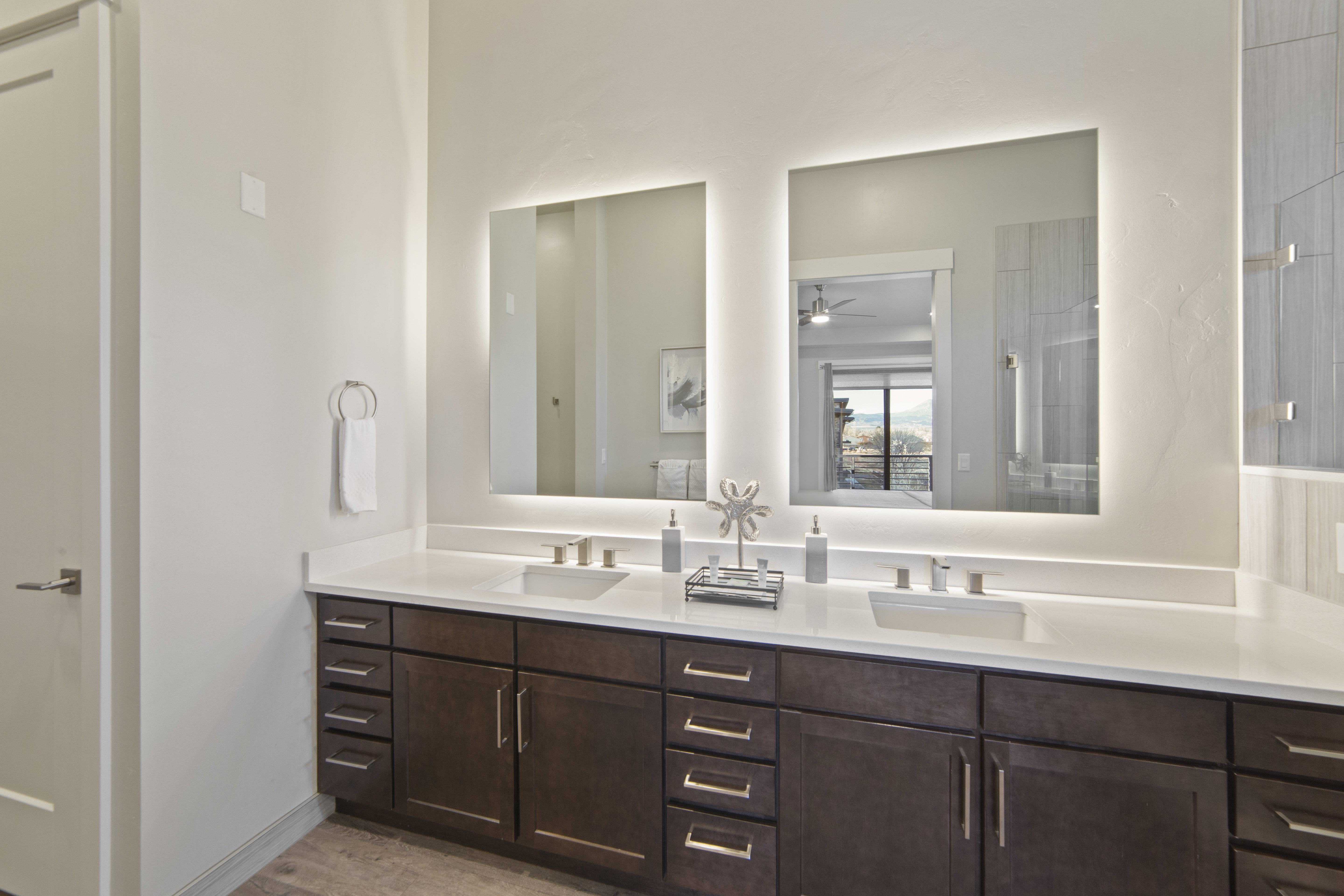 Full bath featuring double vanity, light wood finished floors, tiled shower, and a ceiling fan