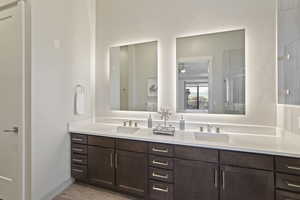 Full bath featuring double vanity, light wood finished floors, tiled shower, and a ceiling fan