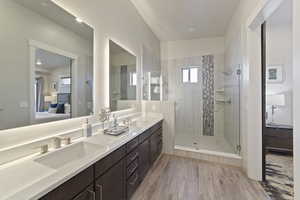 Ensuite bathroom featuring light wood-type flooring, double vanity, and a shower stall