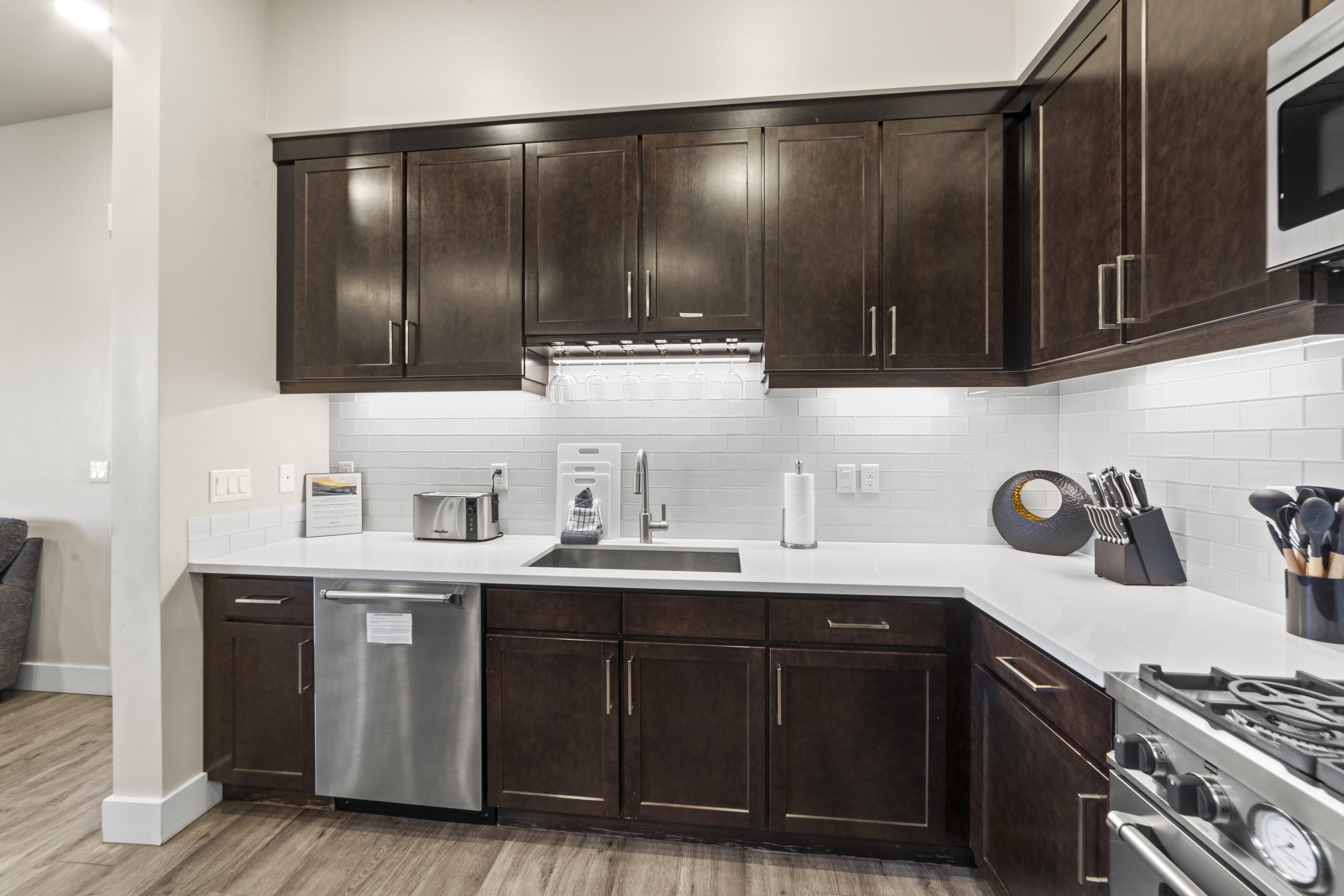 Kitchen with dark brown cabinetry, stainless steel appliances, tasteful backsplash, light wood-style floors, and light stone counters