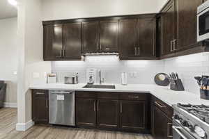 Kitchen with dark brown cabinetry, stainless steel appliances, tasteful backsplash, light wood-style floors, and light stone counters