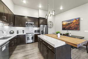 Kitchen featuring dark brown cabinetry, stainless steel appliances, a center island, tasteful backsplash, and pendant lighting