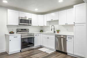 Kitchen featuring stainless steel appliances, white cabinetry, dark wood finished floors, recessed lighting, and light stone countertops