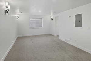 Unfurnished room featuring light carpet, electric panel, and a textured ceiling