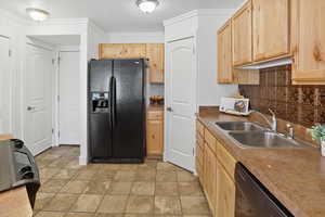 Kitchen with light brown cabinetry, black fridge with ice dispenser, backsplash, dishwashing machine, and crown molding