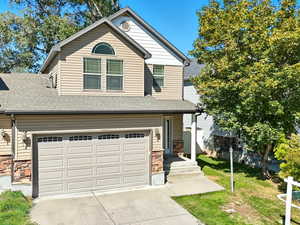 View of front of property featuring stone siding, roof with shingles, concrete driveway, and a garage