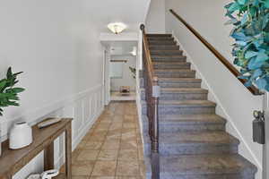 Stairs with wainscoting, ornamental molding, a decorative wall, and tile patterned flooring