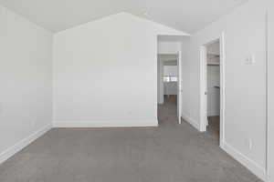 Unfurnished bedroom with a spacious closet, carpet, and vaulted ceiling