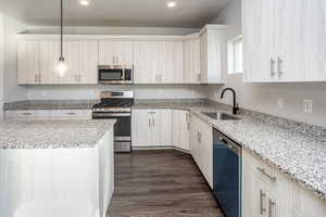 Kitchen with appliances with stainless steel finishes, pendant lighting, light stone countertops, dark wood-style floors, and recessed lighting