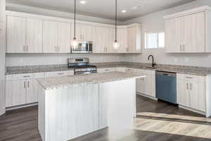 Kitchen featuring light stone countertops, stainless steel appliances, decorative light fixtures, a center island, and dark wood-type flooring