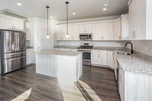 Kitchen with appliances with stainless steel finishes, light stone counters, dark wood-style flooring, a center island, and recessed lighting