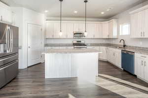 Kitchen featuring appliances with stainless steel finishes, light stone countertops, a center island, hanging light fixtures, and recessed lighting