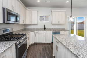Kitchen featuring stainless steel appliances, dark wood finished floors, hanging light fixtures, light stone countertops, and recessed lighting