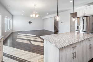 Kitchen featuring hanging light fixtures, stainless steel fridge, light stone counters, dark wood finished floors, and recessed lighting
