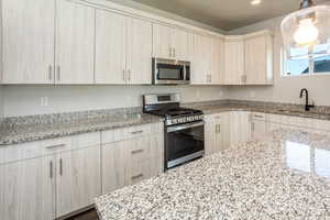 Kitchen featuring stainless steel appliances, light brown cabinets, light stone counters, decorative light fixtures, and recessed lighting