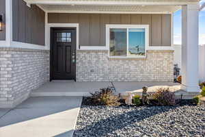 Doorway to property with brick siding, board and batten siding, and covered porch
