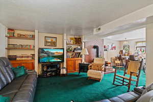 Living room with a wood stove, carpet flooring, and a textured ceiling