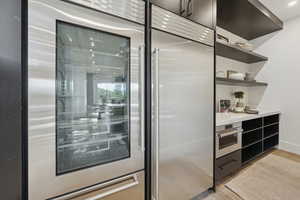 Bar with stainless steel appliances, open shelves, light stone countertops, and beverage cooler