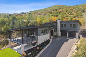 Contemporary house featuring driveway, a wooded view, stone siding, and a chimney
