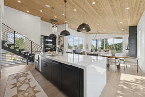 Kitchen with dark cabinets, hanging light fixtures, wood ceiling, light wood-style flooring, and healthy amount of natural light