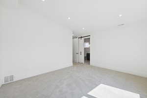 Unfurnished room featuring a barn door, light carpet, and recessed lighting