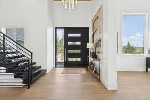 Foyer with light wood-style floors, a chandelier, a high ceiling, and stairs