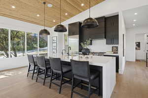 Kitchen with a breakfast bar, decorative light fixtures, dark cabinetry, recessed lighting, and light wood-style flooring