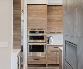 Kitchen with stainless steel double oven, light countertops, light brown cabinetry, modern cabinets, and beverage cooler