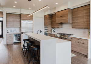 Kitchen with a breakfast bar area, an island with sink, wine cooler, light wood-style floors, and appliances with stainless steel finishes