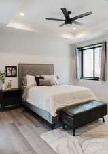 Bedroom with a raised ceiling, recessed lighting, light wood-style flooring, and ceiling fan