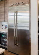 Detailed view of wine cooler, stainless steel built in fridge, light countertops, and dark wood-type flooring