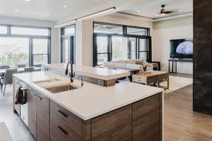 Kitchen featuring dark brown cabinets, light wood-type flooring, a center island with sink, open floor plan, and modern cabinets
