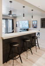 Bar featuring light countertops, light wood-style flooring, hanging light fixtures, vaulted ceiling, and a ceiling fan