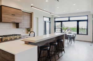Kitchen featuring recessed lighting, decorative backsplash, light wood finished floors, a kitchen breakfast bar, and an island with sink