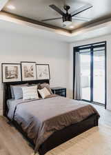 Bedroom with a tray ceiling, light wood-style floors, recessed lighting, access to exterior, and ceiling fan