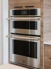 Detailed view of brown cabinetry, stainless steel double oven, and modern cabinets