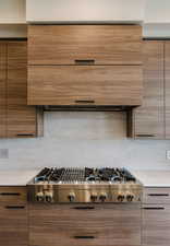 Kitchen featuring brown cabinets, extractor fan, stainless steel gas stovetop, modern cabinets, and decorative backsplash
