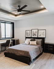 Bedroom featuring a raised ceiling, light wood-style flooring, ceiling fan, and recessed lighting