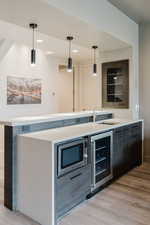 Bar area featuring light wood-style floors, wine cooler, modern cabinets, decorative light fixtures, and light stone countertops