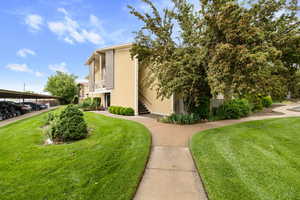 View of side of home with stairway, a lawn, stucco siding, and a balcony