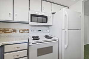 Kitchen with white appliances, white cabinetry, and carpet floors