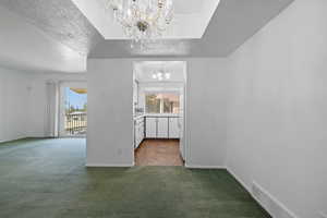 Spare room featuring a textured ceiling, dark carpet, and a chandelier