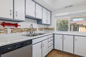 Kitchen featuring stainless steel dishwasher, light countertops, decorative backsplash, white cabinets, and dark stone finish floors