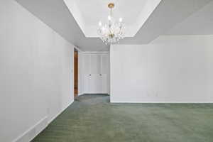Unfurnished dining area with a chandelier, carpet flooring, a raised ceiling, and a textured ceiling