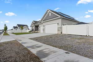View of side of home with concrete driveway, stone siding, stucco siding, an attached garage, and solar panels